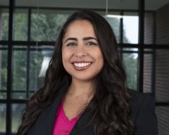 Ana Gabriela de Oliveira Rosa in a pink top and black blazer, stands in front of a window and smiles.