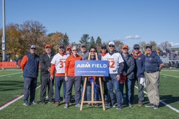 Members of ABM and Utica University stand on the football field by a sign that says "ABM Field."