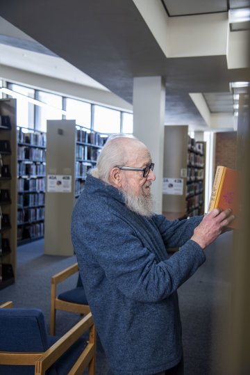 Professor John Cormican pulls a book from a shelf in the Utica University Library.
