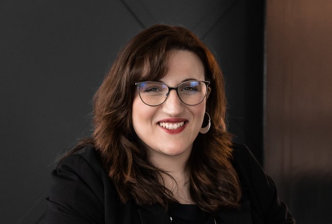 Francesca Orsomarso in glasses and black top, sits at a table, with hands on a laptop.