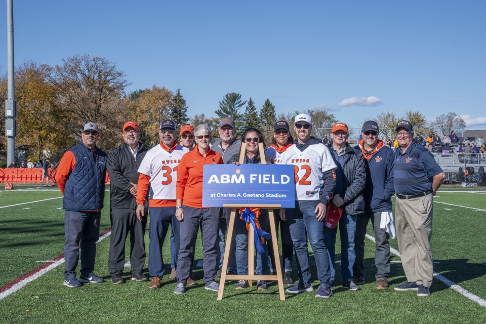 Members of ABM and Utica University stand on the football field by a sign that says "ABM Field."